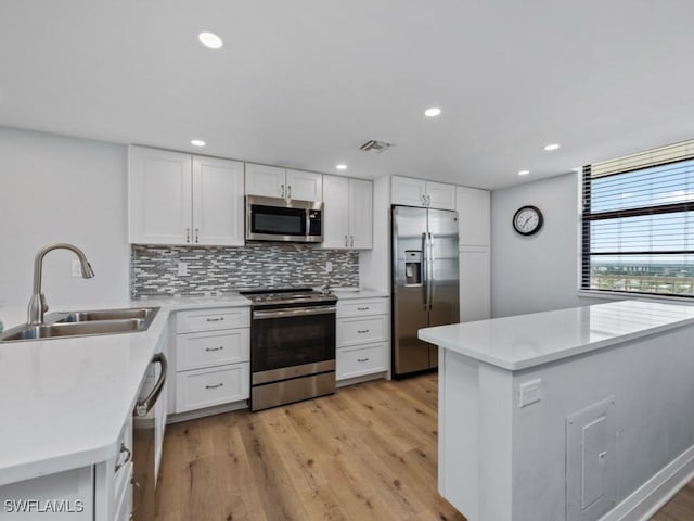 kitchen with visible vents, decorative backsplash, a sink, light wood finished floors, and stainless steel appliances