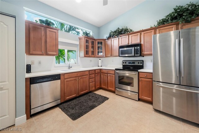 kitchen with appliances with stainless steel finishes, a sink, light countertops, brown cabinets, and glass insert cabinets