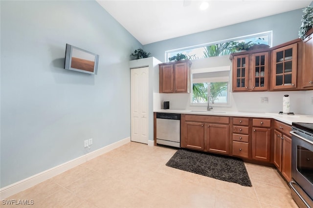 kitchen with stainless steel appliances, a sink, light countertops, glass insert cabinets, and lofted ceiling