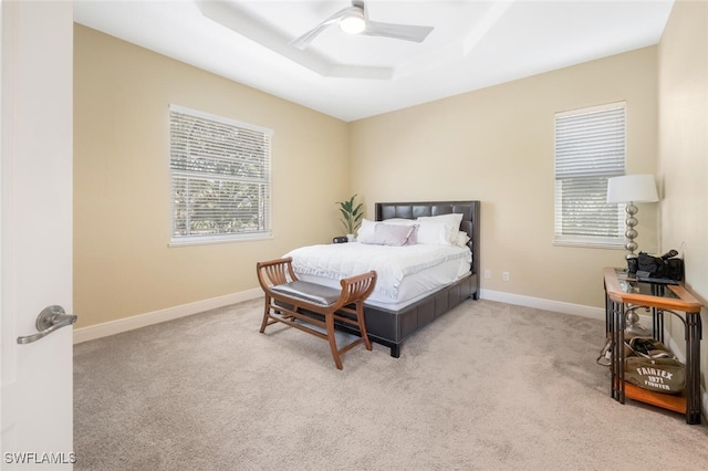 carpeted bedroom with a tray ceiling, baseboards, and ceiling fan