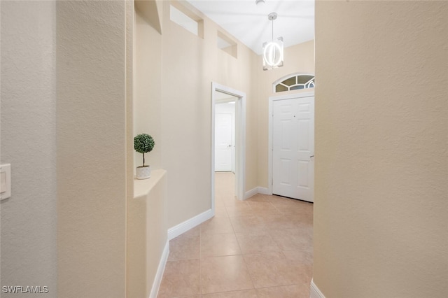 hallway with light tile patterned flooring, a textured wall, and baseboards