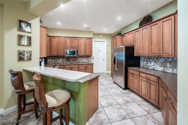 kitchen featuring stainless steel appliances, a kitchen bar, tasteful backsplash, a peninsula, and brown cabinets