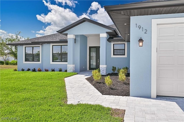 view of front facade featuring a garage, a shingled roof, a front yard, and stucco siding