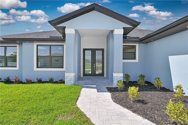 view of exterior entry with a lawn, roof with shingles, stucco siding, and french doors