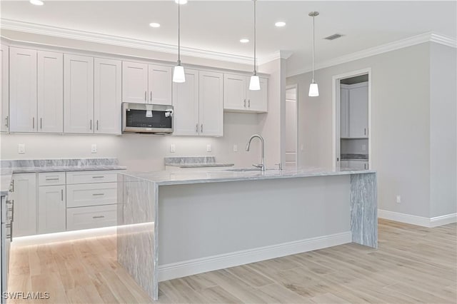 kitchen with a sink, light wood finished floors, stainless steel microwave, visible vents, and ornamental molding