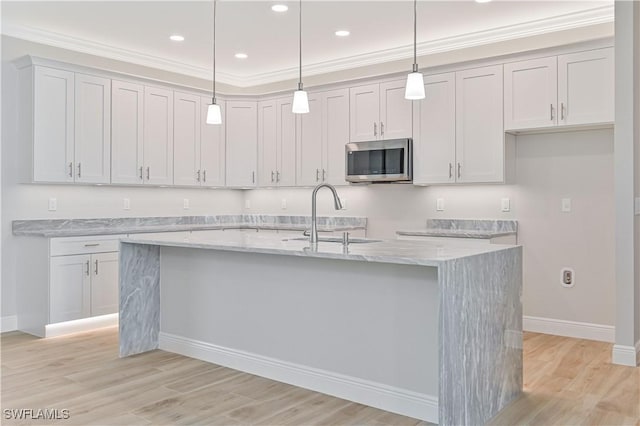 kitchen with baseboards, stainless steel microwave, a sink, and a kitchen island with sink