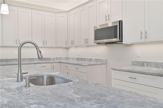 kitchen featuring crown molding, light stone countertops, stainless steel microwave, a sink, and decorative light fixtures
