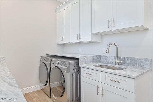 clothes washing area featuring cabinet space, a sink, baseboards, light wood-style flooring, and washer and clothes dryer