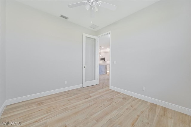 spare room featuring visible vents, a ceiling fan, light wood-style floors, and baseboards