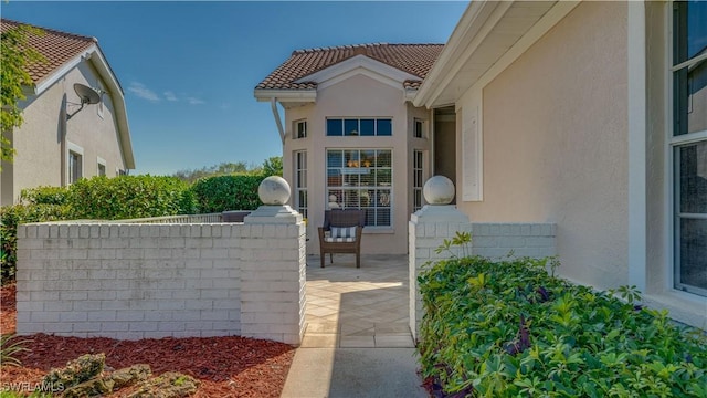 doorway to property featuring a patio, stucco siding, a tiled roof, and fence