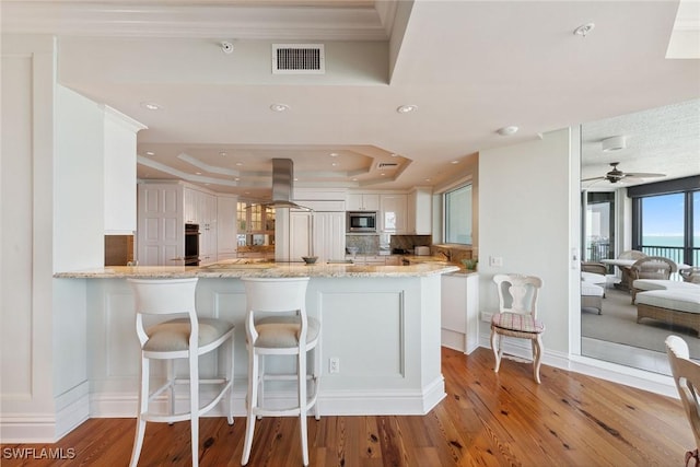 8477 Bay Colony Dr Unit 1102, Naples, FL 34108 - kitchen featuring island range hood, visible vents, a raised ceiling, stainless steel microwave, and a peninsula