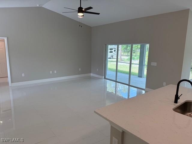 unfurnished living room featuring baseboards, a sink, ceiling fan, and lofted ceiling