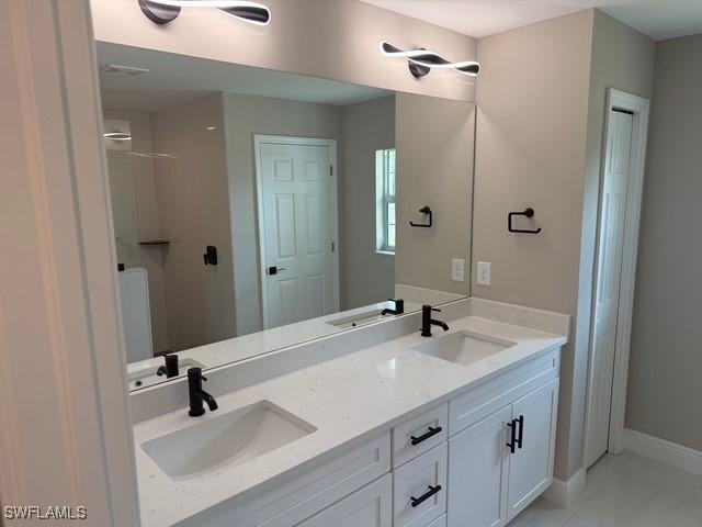bathroom featuring a sink, baseboards, walk in shower, and double vanity