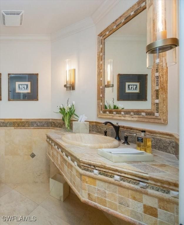 bathroom with a sink, crown molding, tile walls, tile patterned flooring, and a wainscoted wall