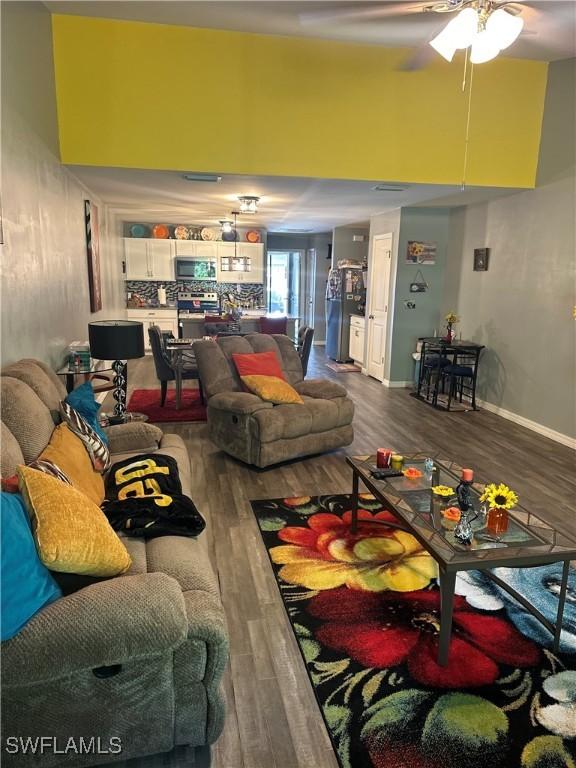 living area featuring a ceiling fan, a high ceiling, and wood finished floors