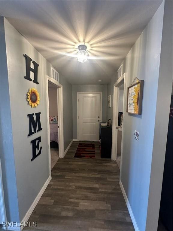 corridor with visible vents, baseboards, and dark wood-style floors