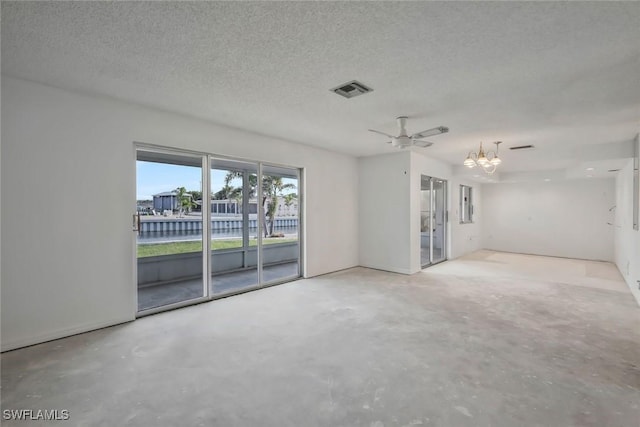 spare room with a textured ceiling, visible vents, concrete floors, and ceiling fan with notable chandelier