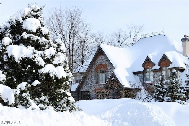view of snow covered exterior featuring a chimney and stone siding