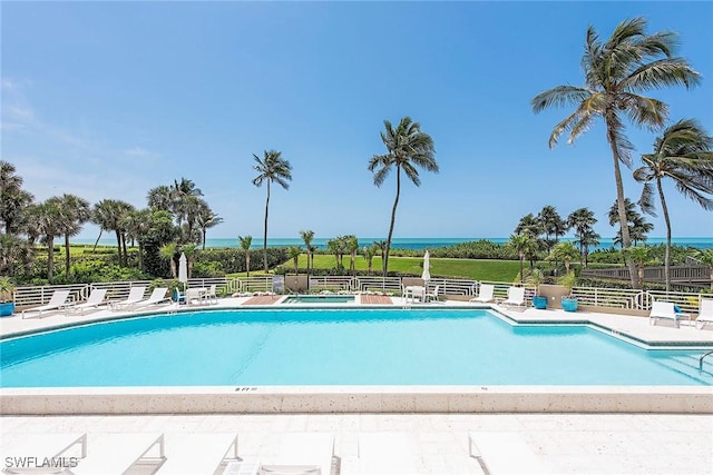 community pool with fence, a patio, and a water view