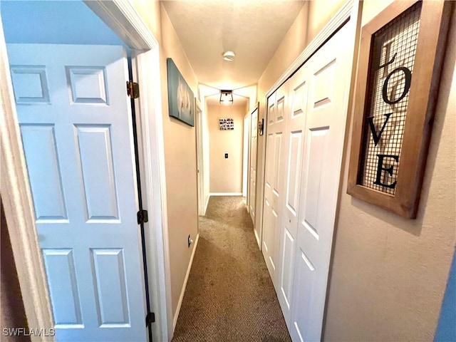 corridor with baseboards and dark colored carpet