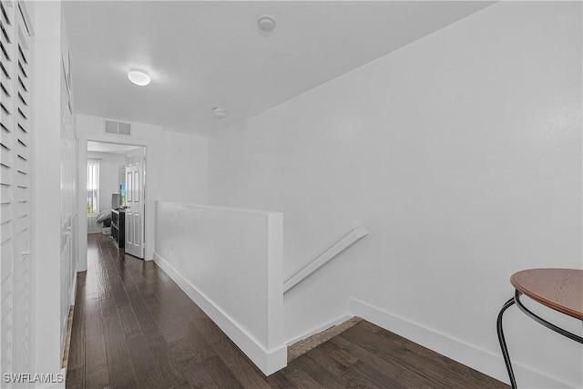 hallway with baseboards, visible vents, wood finished floors, and an upstairs landing