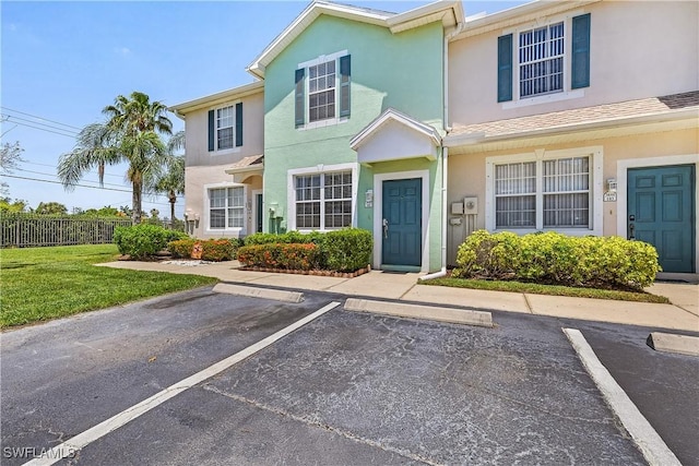 view of property with stucco siding, uncovered parking, fence, and a front yard