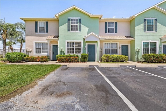view of property featuring a front lawn, uncovered parking, and stucco siding