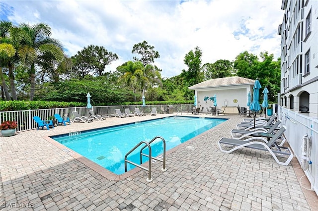 community pool featuring fence, an outdoor structure, and a patio area