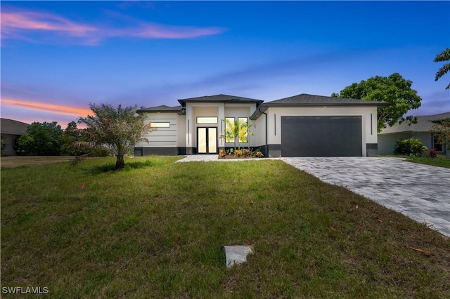 prairie-style home with a garage, decorative driveway, stucco siding, french doors, and a lawn