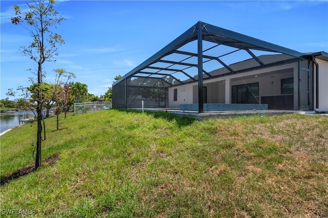 back of property featuring a lawn, a water view, and a lanai