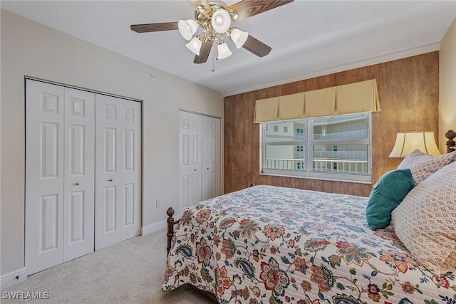 bedroom featuring wooden walls, multiple closets, a ceiling fan, and carpet flooring