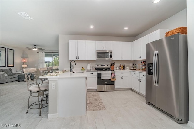 kitchen with visible vents, a peninsula, open floor plan, a sink, and stainless steel appliances