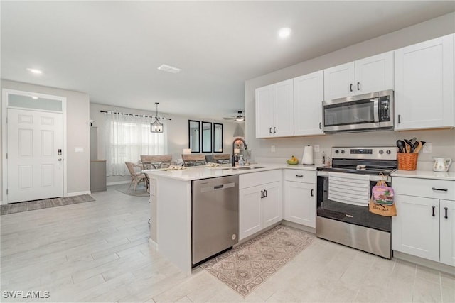 kitchen featuring appliances with stainless steel finishes, a sink, light countertops, white cabinets, and a peninsula