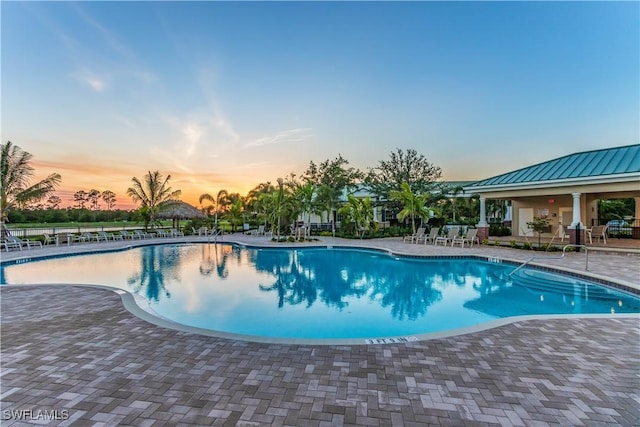 pool at dusk with a community pool and a patio