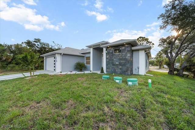 prairie-style home with an attached garage, a front lawn, stucco siding, and stone siding