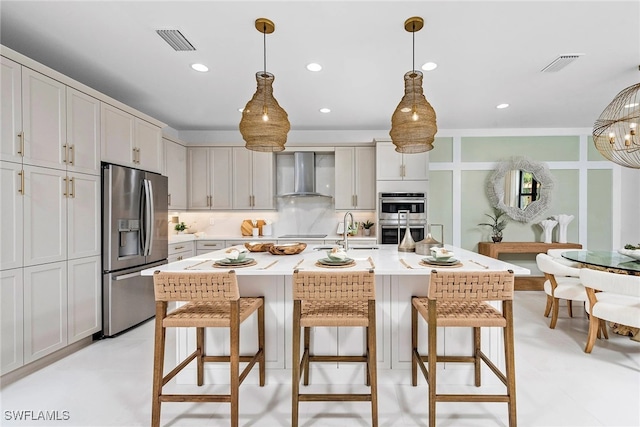 kitchen with visible vents, wall chimney exhaust hood, a kitchen bar, and stainless steel appliances