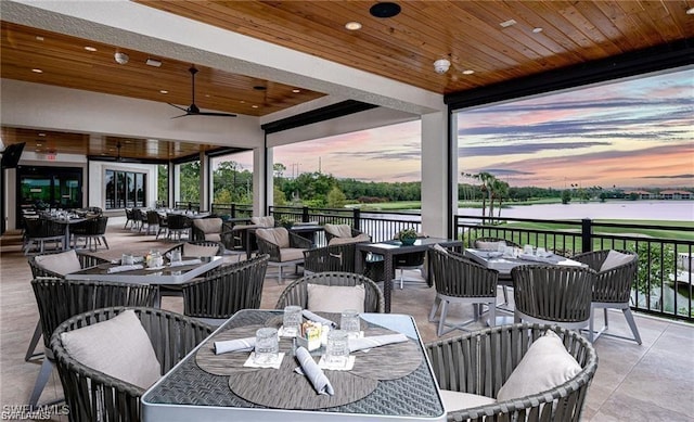 patio terrace at dusk featuring a water view, a ceiling fan, outdoor dining area, and an outdoor living space