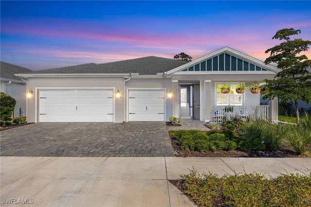 ranch-style home featuring covered porch, decorative driveway, an attached garage, and stucco siding