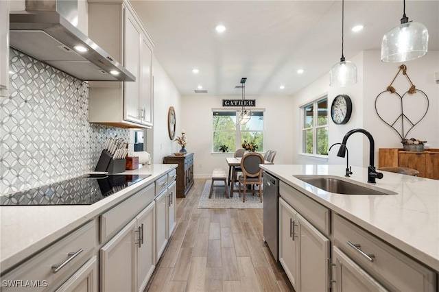 kitchen with decorative backsplash, wall chimney range hood, a sink, light wood finished floors, and dishwasher