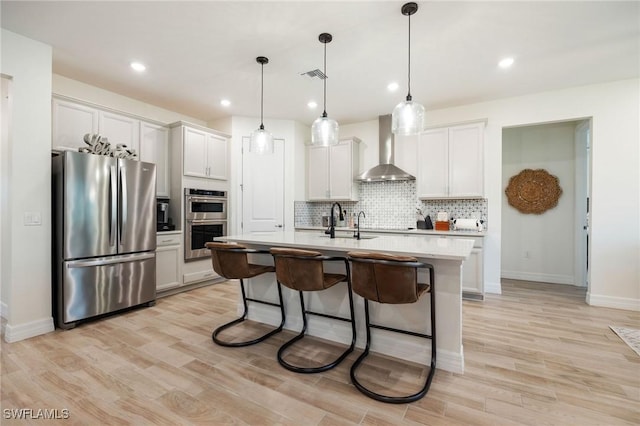 kitchen featuring visible vents, decorative backsplash, wall chimney exhaust hood, a sink, and appliances with stainless steel finishes