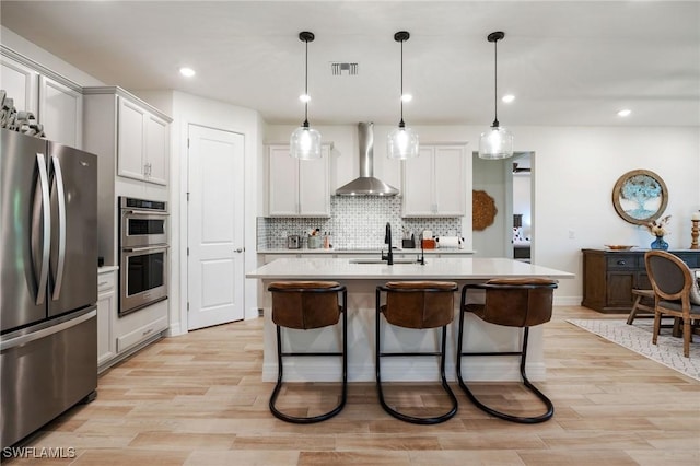 kitchen featuring visible vents, wall chimney range hood, light countertops, a sink, and appliances with stainless steel finishes