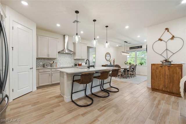 kitchen with wall chimney range hood, light wood finished floors, a sink, and visible vents