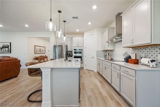 kitchen with wall chimney range hood, a kitchen bar, visible vents, appliances with stainless steel finishes, and open floor plan