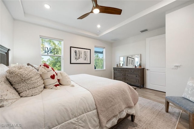 bedroom with a raised ceiling, multiple windows, and light wood finished floors