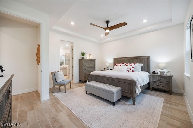 bedroom featuring recessed lighting, baseboards, ensuite bathroom, light wood-type flooring, and a tray ceiling