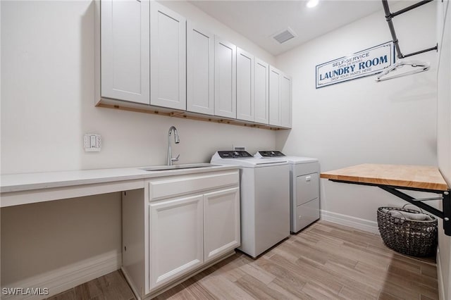 laundry room with washing machine and clothes dryer, light wood-type flooring, cabinet space, a sink, and baseboards