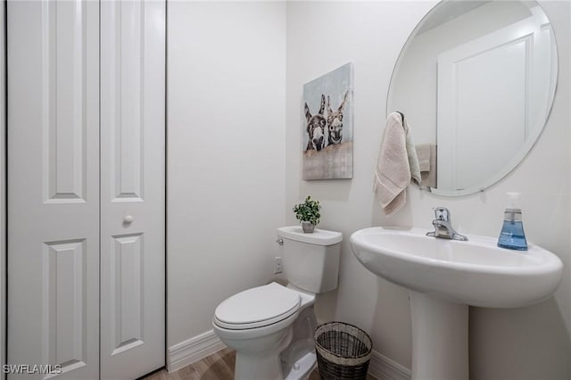 half bathroom with toilet, baseboards, a sink, and wood finished floors