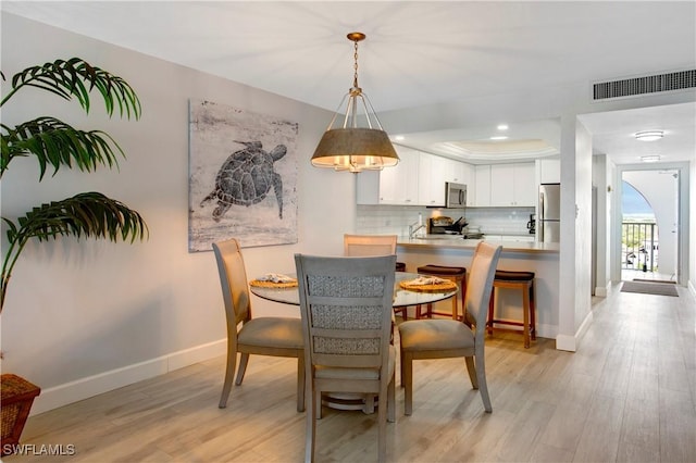 dining room with light wood-style floors, a raised ceiling, baseboards, and visible vents