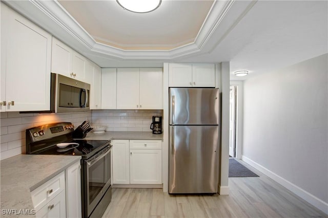 kitchen featuring appliances with stainless steel finishes, white cabinets, a tray ceiling, and tasteful backsplash