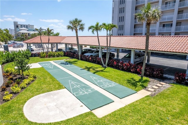 view of community with a lawn, covered and uncovered parking, and shuffleboard